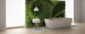 greenery wall behind a soaking tub places on white pebbles and a stool next to it with white fluffy towels