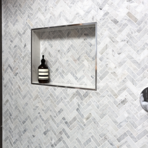 shower tiled in marble herringbone pattern featuring a shower niche