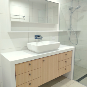 vanity unit with beech veneer cupboards and drawers, white stone bench tops, white, rectangular on-top basin and mirrored shaving cabinets