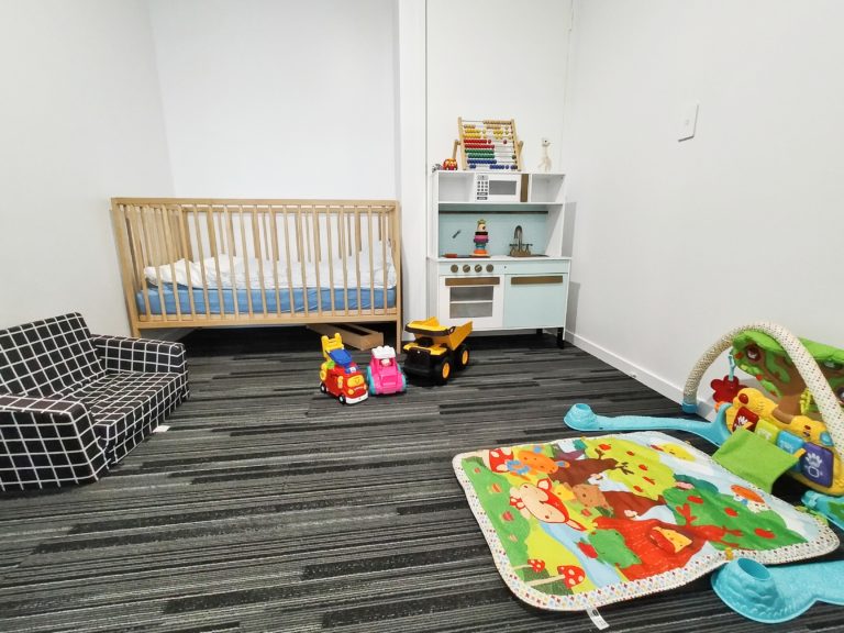 Playroom at Nyblad Construction with black carpet, cot on back wall with play kitchen and bay toys on the floor