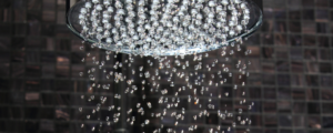 close up of rain shower head with close up water droplets contrasted against square black mosaic tiles
