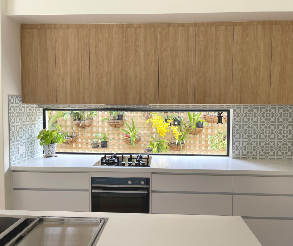 Kitchen image: over head cabinets in a light wood grain hanging over a window splashback with white stone benchtops and white drawers and gas cooktop