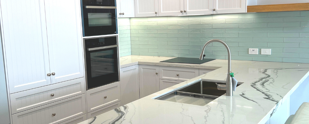 white kitchen with country cabinets, aqua subway tiles and white stone benchtop with grey marble pattern.